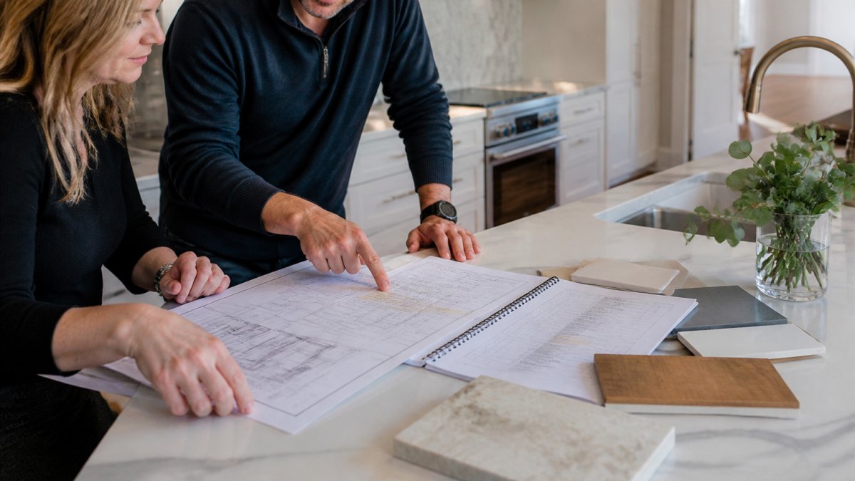 Homeowner and builder reviewing plans for a luxury custom renovation at a kitchen island in a bright home.