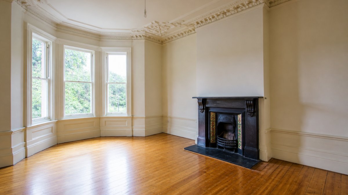 Interior of a period home showing original architectural details including ornate ceiling cornicing, polished timber floorboards, and a heritage fireplace with decorative tiles before renovation work begins